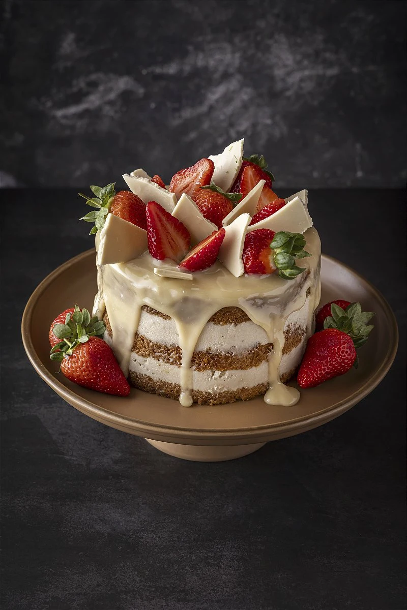 Bolo de ganache branca decorado com morangos e folhagens